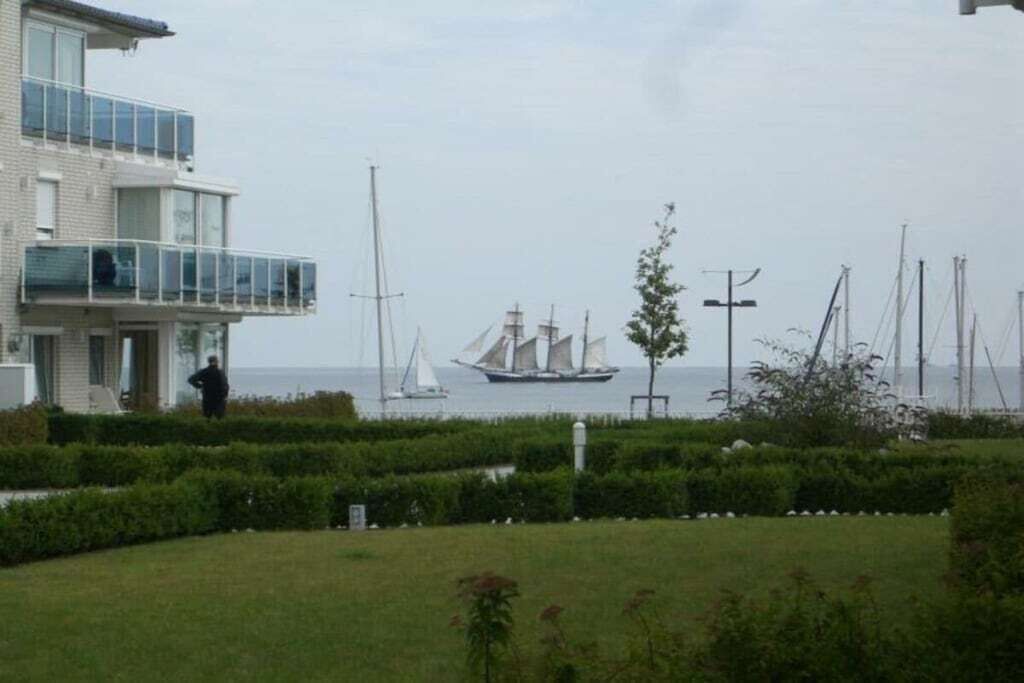 A modern building with a balcony overlooking a grassy area and a body of water with sailboats.