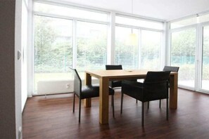 A dining area with a table and chairs, large windows, and a view of greenery. - Holiday apartment at the marina 319704 (Kühlungsborn)