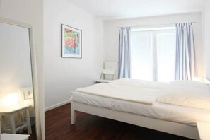 A bedroom with a bed, a chair, a desk, and a window with curtains. - Holiday apartment at the marina 319704 (Kühlungsborn)