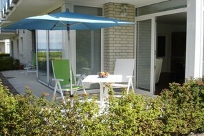 A patio with a table and chairs, a blue umbrella, and a view of the outdoors. - Holiday apartment at the marina 319704 (Kühlungsborn)