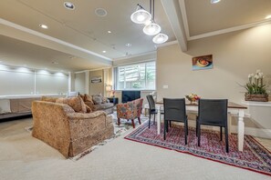 A spacious living room with a patterned sofa, a dining area with chairs and a table, and a large window providing natural light. - Full Kitchen & Laundry! Kirkland Studio Suite (Kirkland)