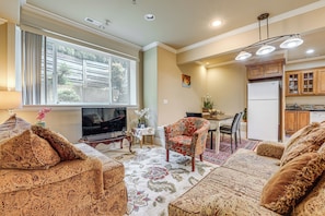 A living room with a television, a dining table, and a kitchen area with cabinets and a refrigerator. - Full Kitchen & Laundry! Kirkland Studio Suite (Kirkland)