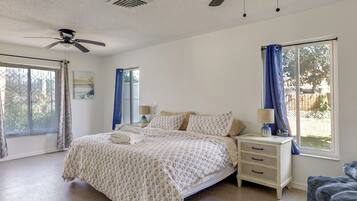 A bedroom with a bed, nightstand, lamp, ceiling fan, and large windows.