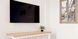 A television mounted on a wall with a plant on a wooden console below. - Studio cosy au cœur du Haut-Marais – Calme & Élégance • 2 personnes (Paris)