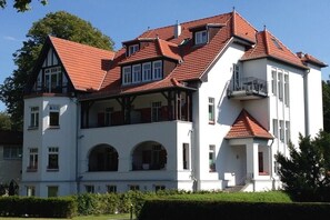 A large, multi-story building with a red-tiled roof, multiple balconies, and a prominent entrance with a staircase. - Holiday apartment Villa Löwenstein 319575 (Kühlungsborn)