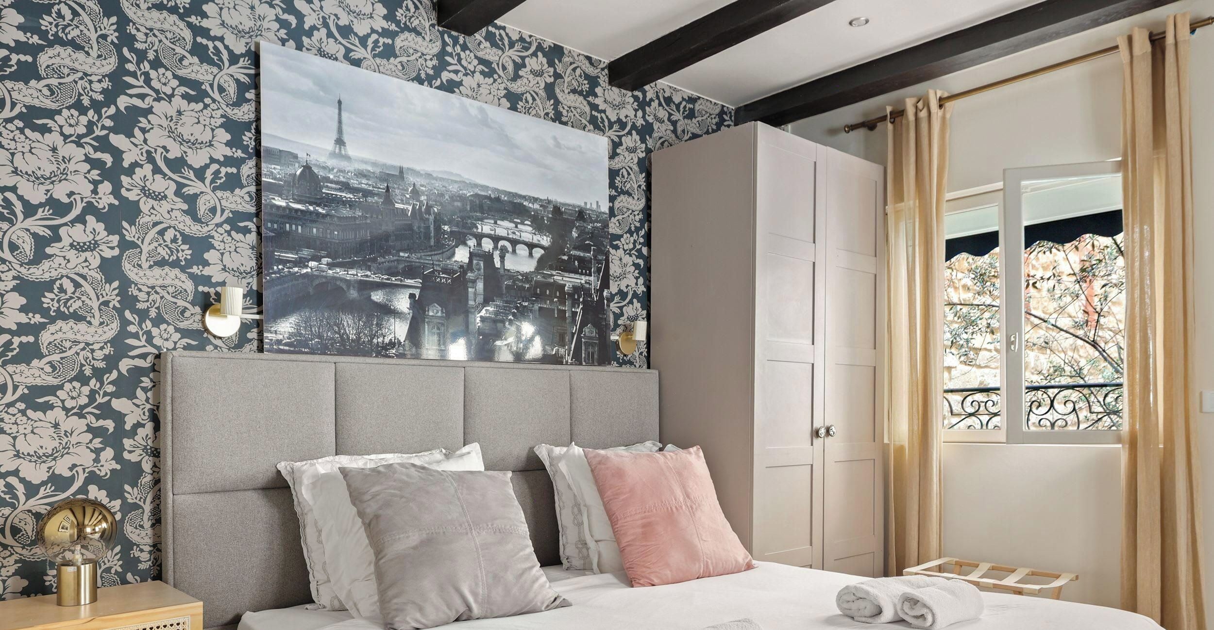 A bedroom with a bed, pillows, a nightstand, a wall-mounted picture, and a wardrobe.