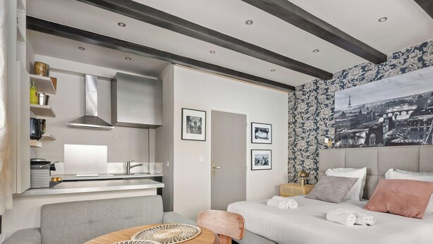 A modern living room with a sofa, a dining area with a kitchen, and a cityscape view. - Charmante maison au cœur de Paris – Face au Louvre • 2 personnes (Paris)