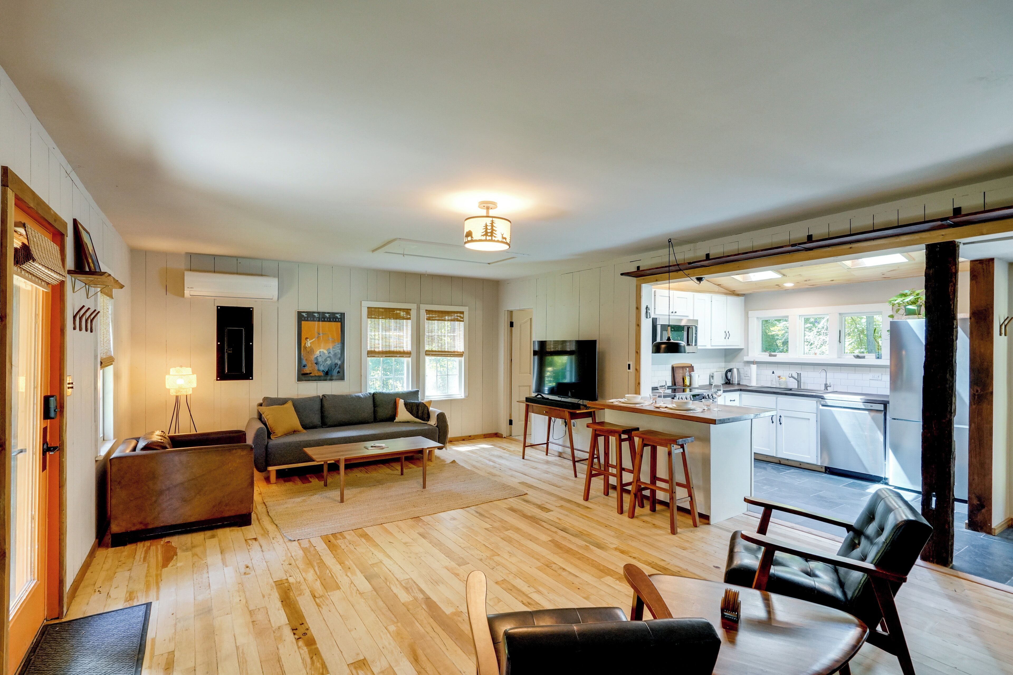 A modern living room with a sofa, coffee table, and a TV. There is a kitchen area with a dining table and bar stools.