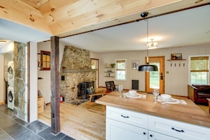 A spacious kitchen with a stone fireplace, wooden beams, and a dining area with a table set for two.