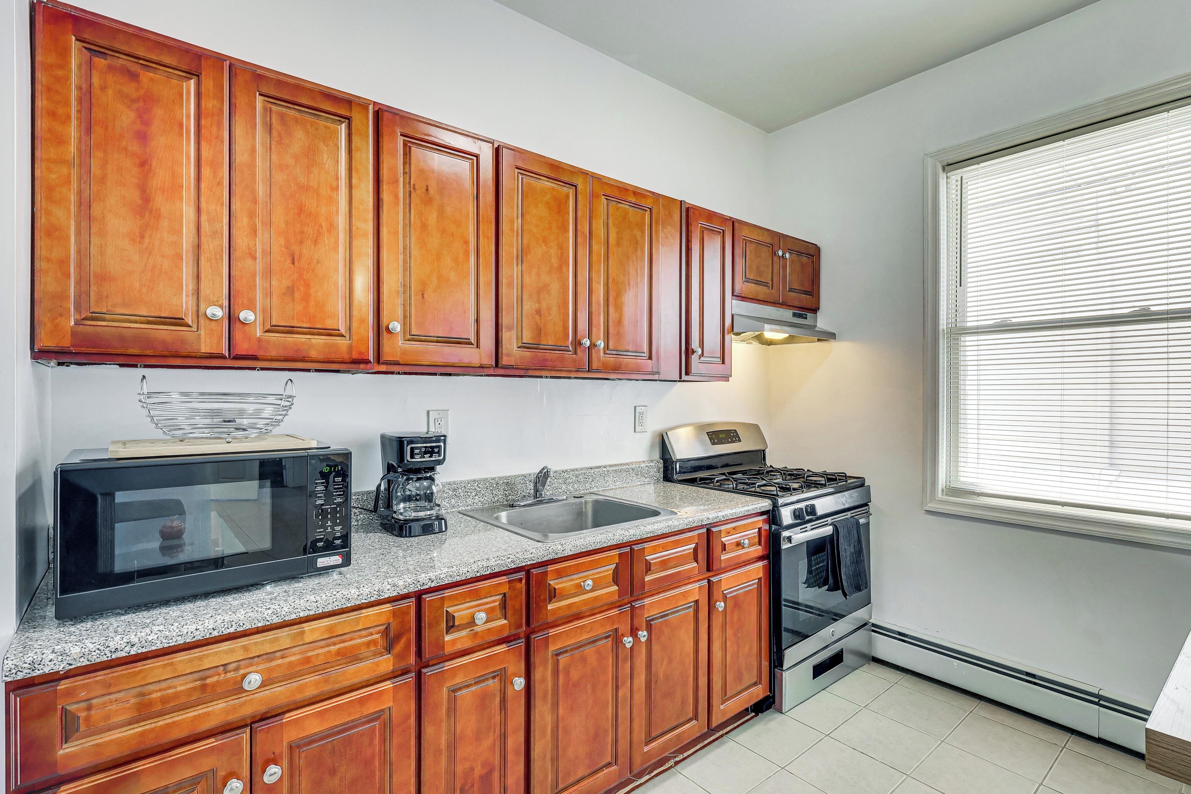 A kitchen with wooden cabinets, a microwave, a coffee maker, a stove, and a window with blinds.