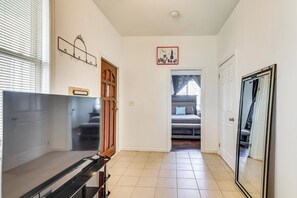 A hallway with a bed, a door, a coat rack, and a clock on the wall.