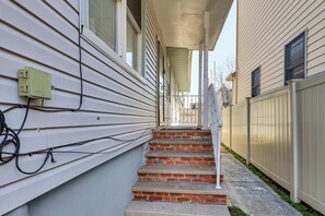 Fachada residencial com escadaria de tijolos que leva a um alpendre, parede externa branca e cerca.