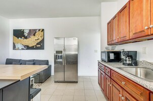 Una cocina moderna con electrodomésticos de acero inoxidable, armarios de madera y un comedor con sofá gris.