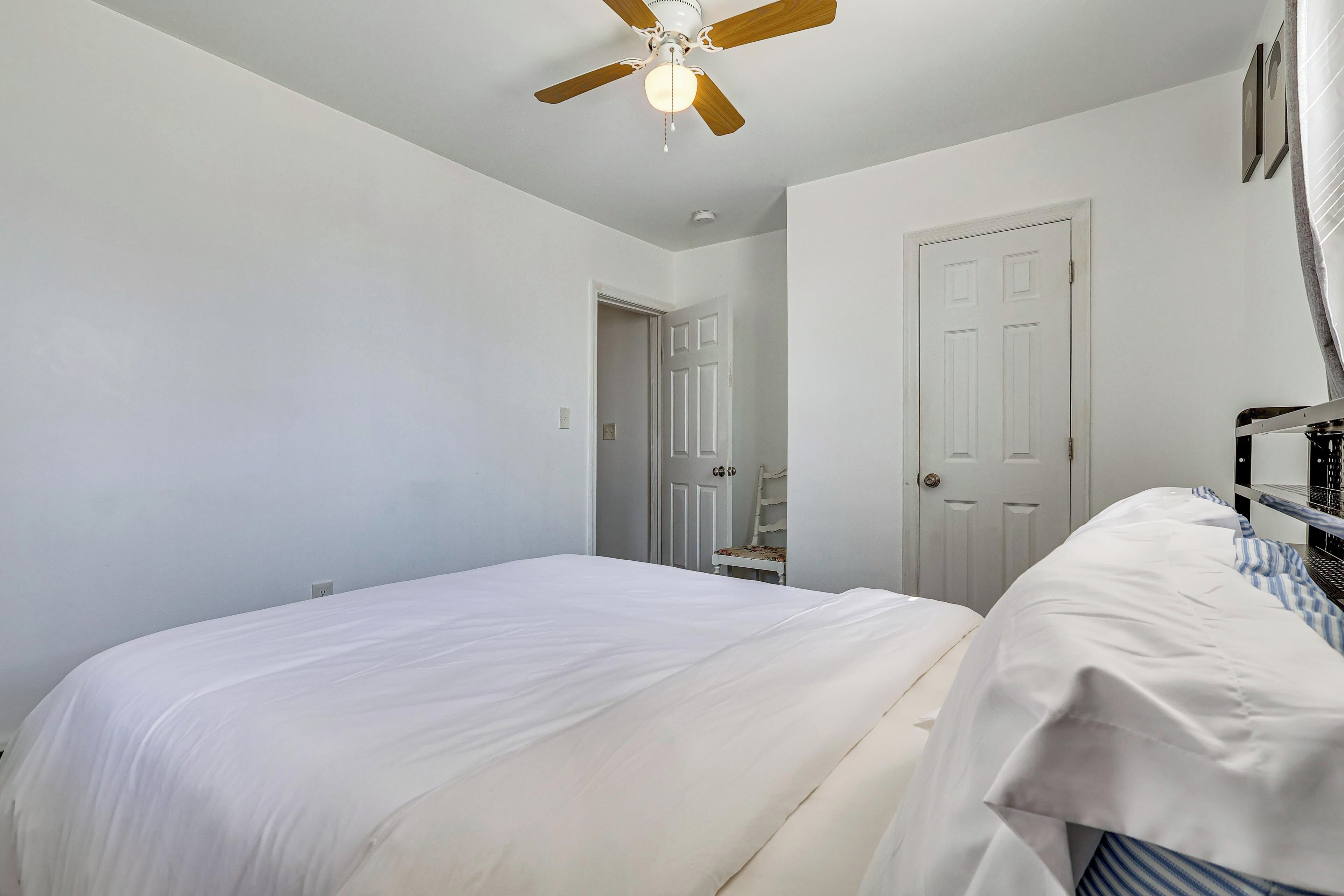 A bedroom with a bed, a ceiling fan, a door, and a window.