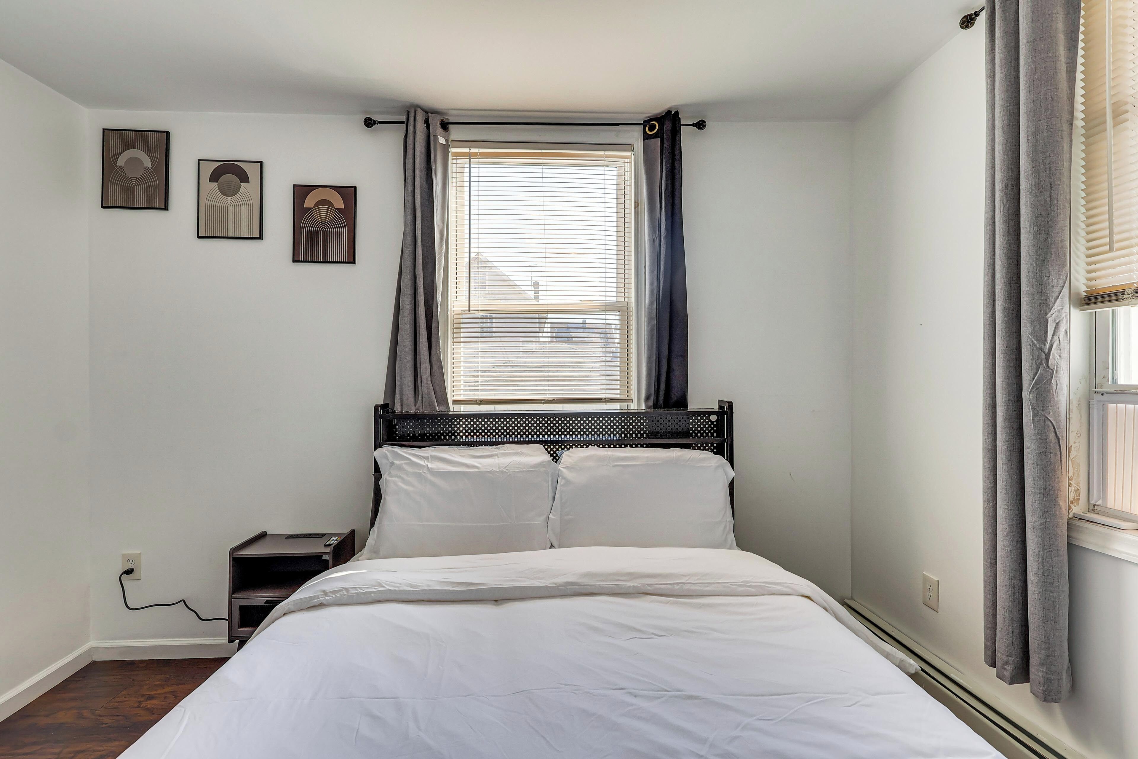 Quarto com cama, mesa de cabeceira, janela com persianas e três obras de arte na parede.