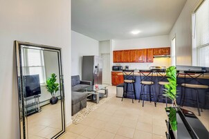 Un espacio habitable compacto con kitchenette, una zona de comedor con taburetes de bar, un sofá y un espejo grande.