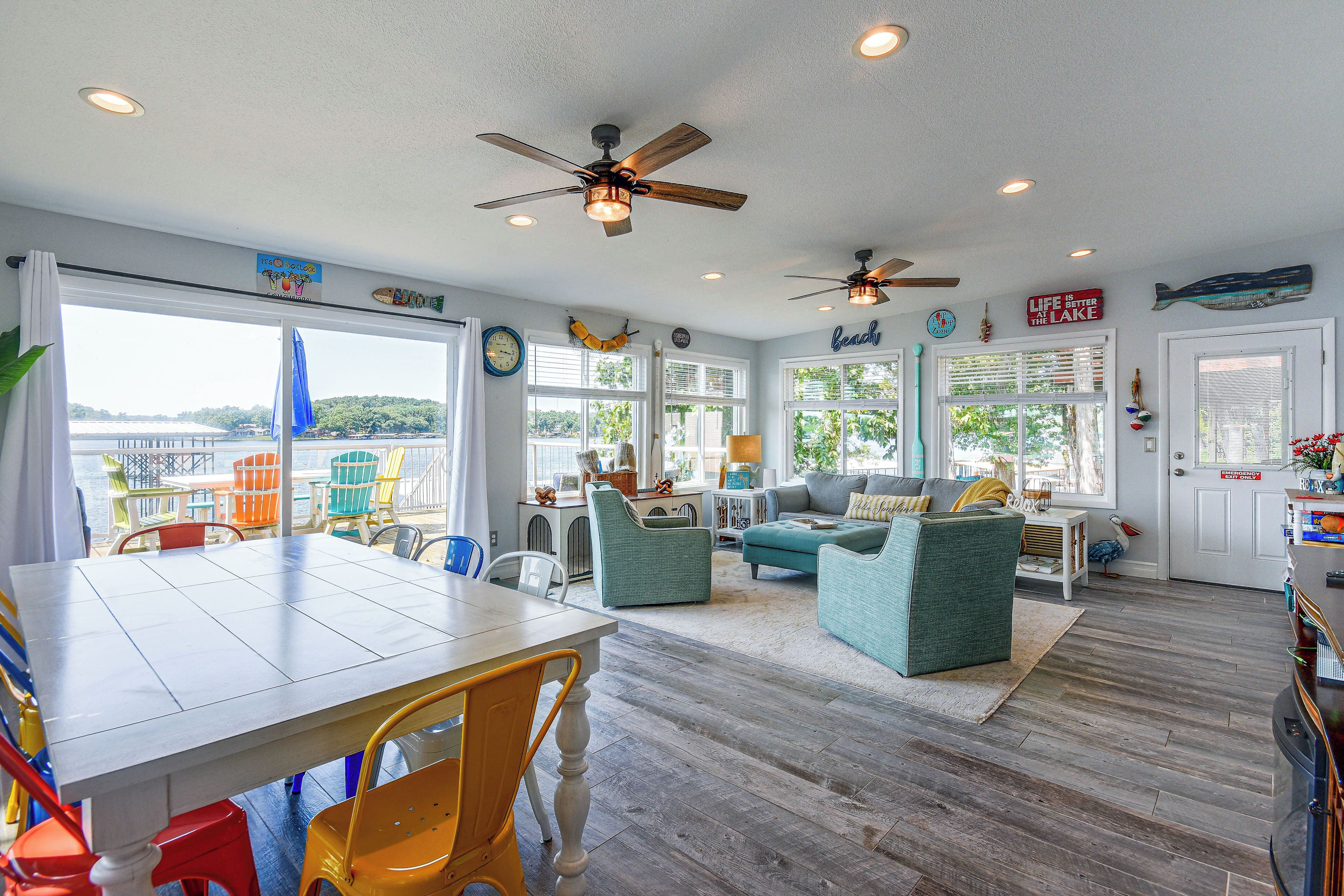 A spacious living area with a large window overlooking a dock, a dining table with chairs, and a cozy seating area with a sofa and armchairs.