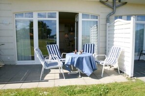 Eine Außenpatio mit Tisch und vier gestreiften Stühlen, ein überdachter Bereich mit einer Tür sowie eine weiße Außenwand.