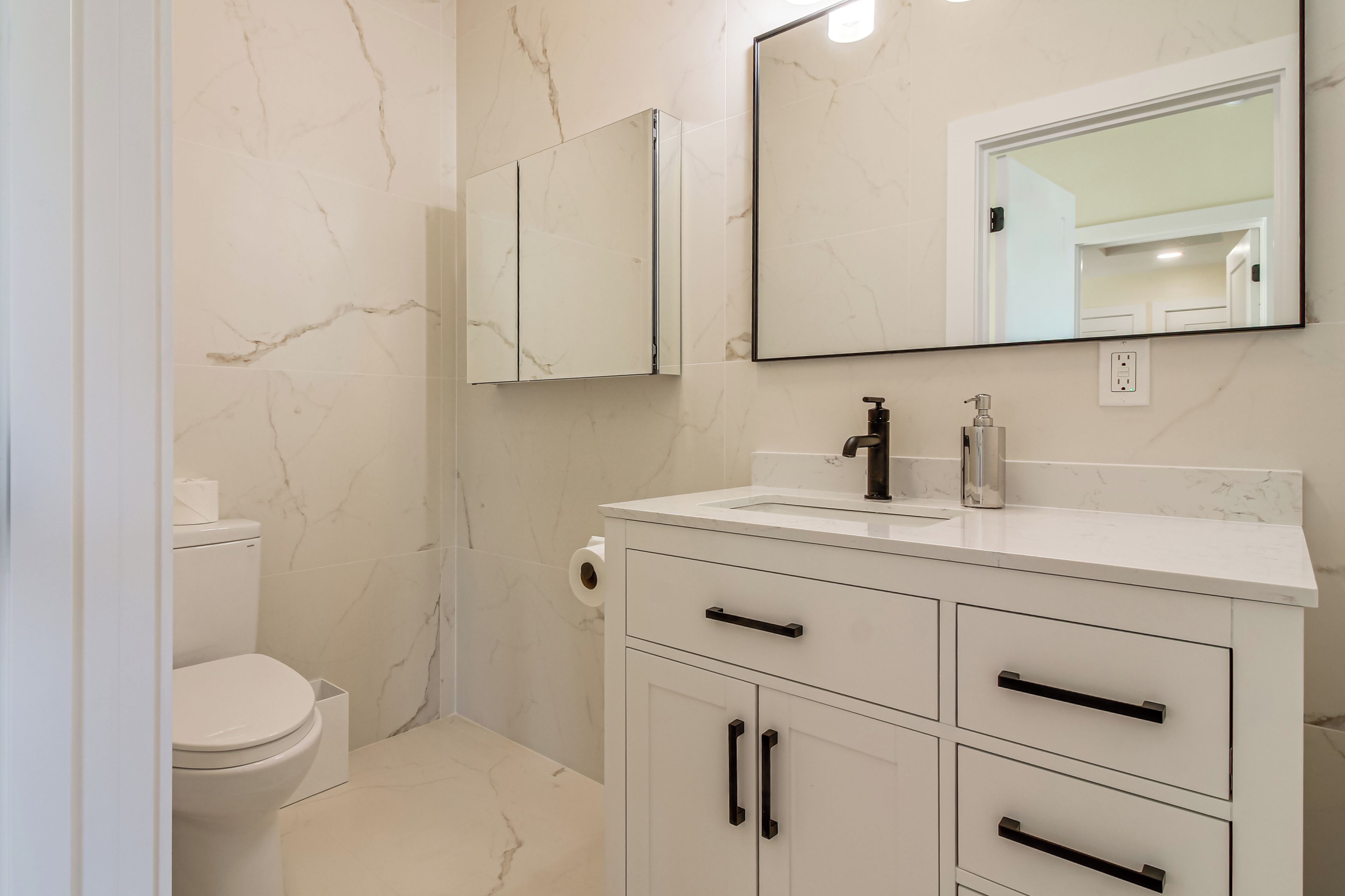 A bathroom with a toilet, a sink, a mirror, and a cabinet.