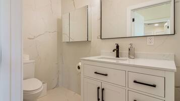 A bathroom with a toilet, a sink, a mirror, and a cabinet.