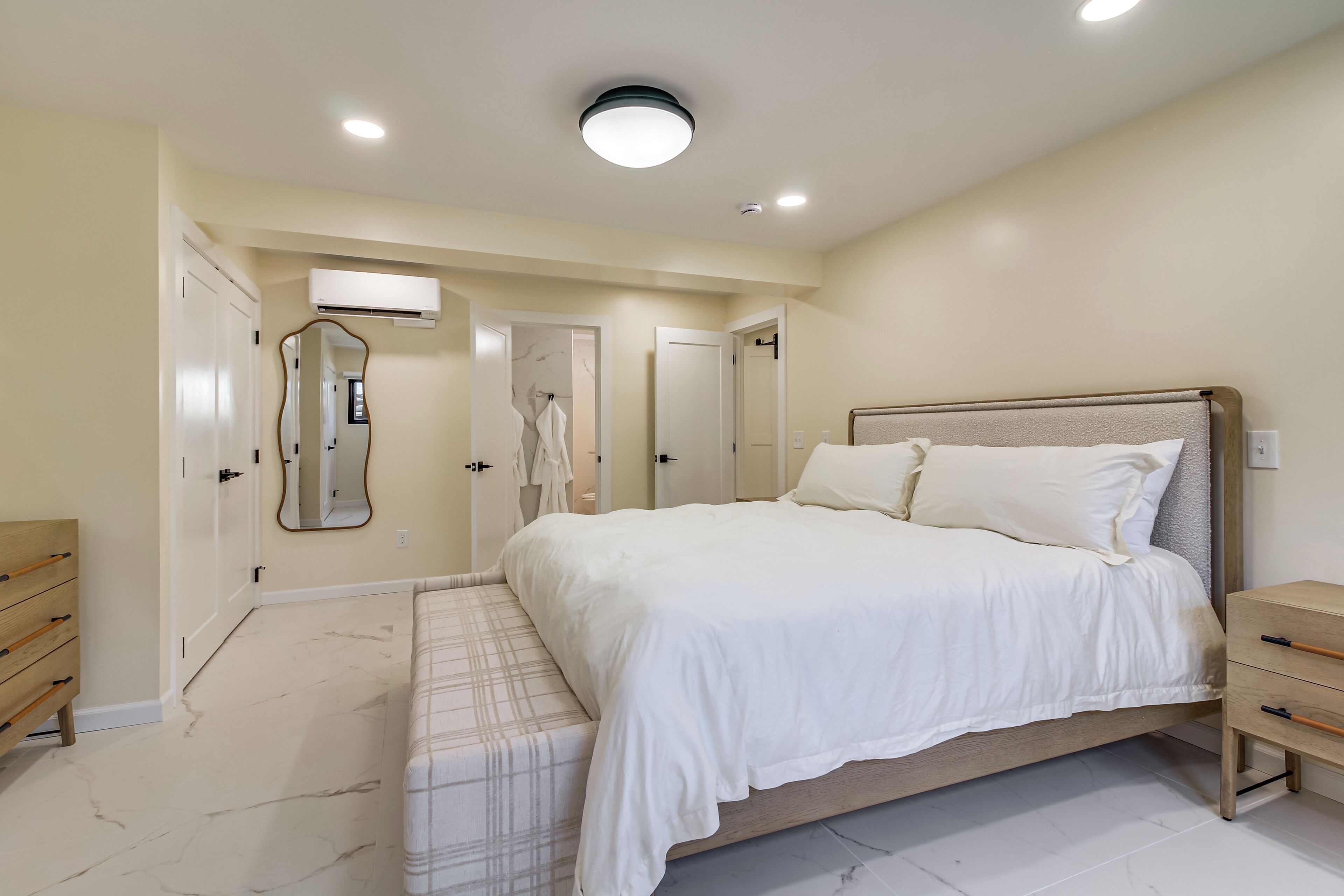 A bedroom with a bed, bedside tables, a mirror, and a door leading to another room.