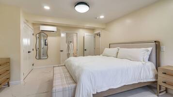 A bedroom with a bed, bedside tables, a mirror, and a door leading to another room.