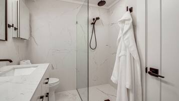 A modern bathroom with a glass-enclosed shower, a white marble sink, and a white bathrobe hanging on the door.