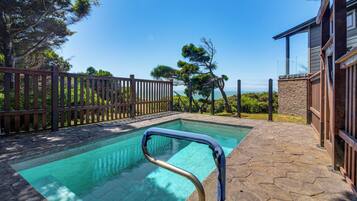 A swimming pool with a wooden deck and stone tiles, surrounded by a wooden fence and trees.