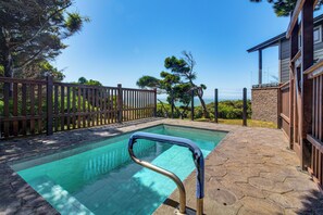 A swimming pool with a wooden deck and stone tiles, surrounded by a wooden fence and trees.