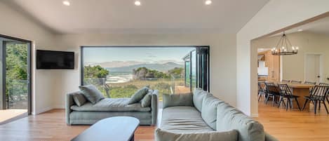 A modern living room with a large window, a sofa, a coffee table, and a dining area with chairs.