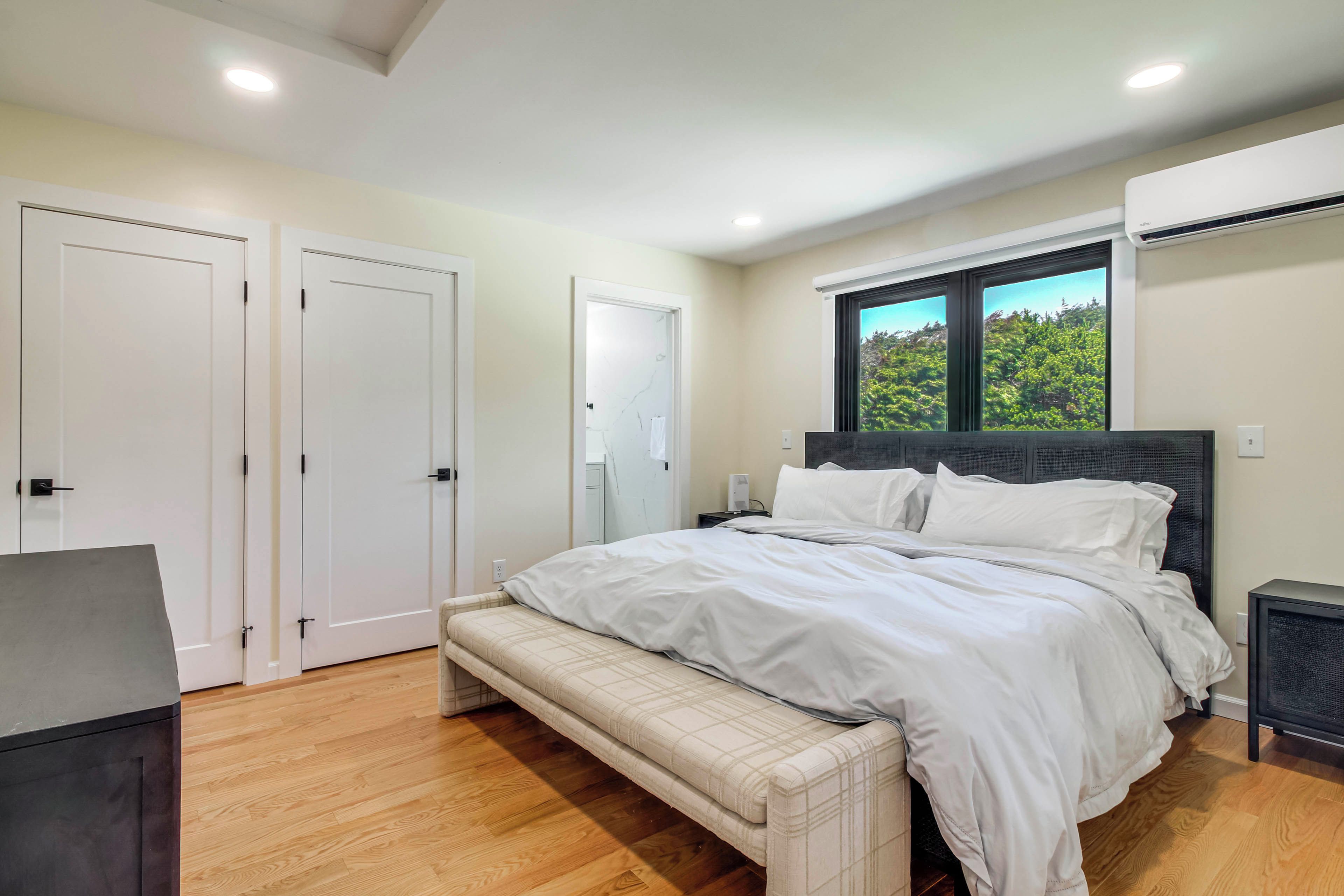 A bedroom with a bed, bench, wardrobe, and an air conditioning unit.