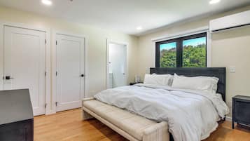 A bedroom with a bed, bench, wardrobe, and an air conditioning unit.
