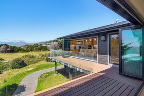 A modern house with a glass balcony overlooking a landscaped garden and distant mountains. - Beachfront, Pool, and Views on Oregon Coast: 5BR (Gold Beach)