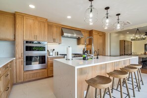 A modern kitchen with wooden cabinets, stainless steel appliances, a central island with stools, and pendant lighting. - Beachfront, Pool, and Views on Oregon Coast: 5BR (Gold Beach)