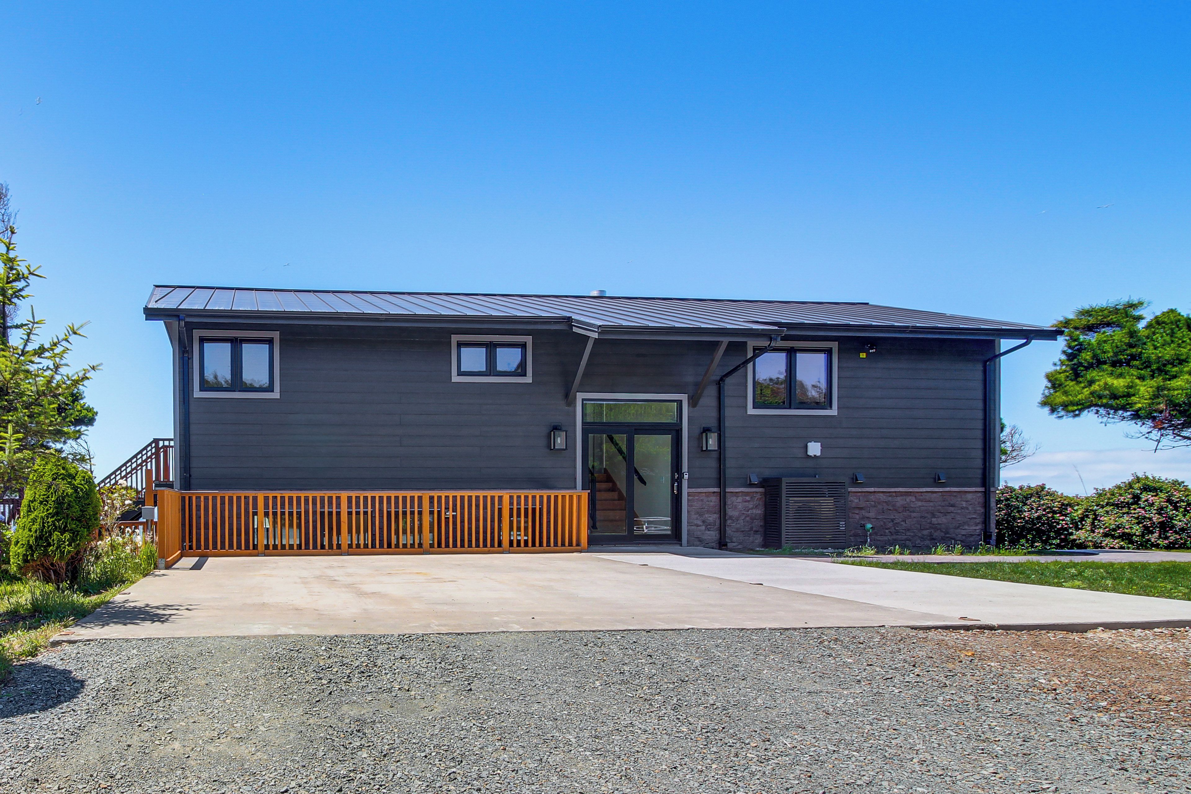 A modern two-story house with a dark exterior, a wooden deck, and a clear sky.