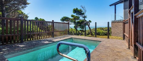 Una piscina con cubierta de madera y baldosas de piedra, rodeada por una valla de madera y árboles.