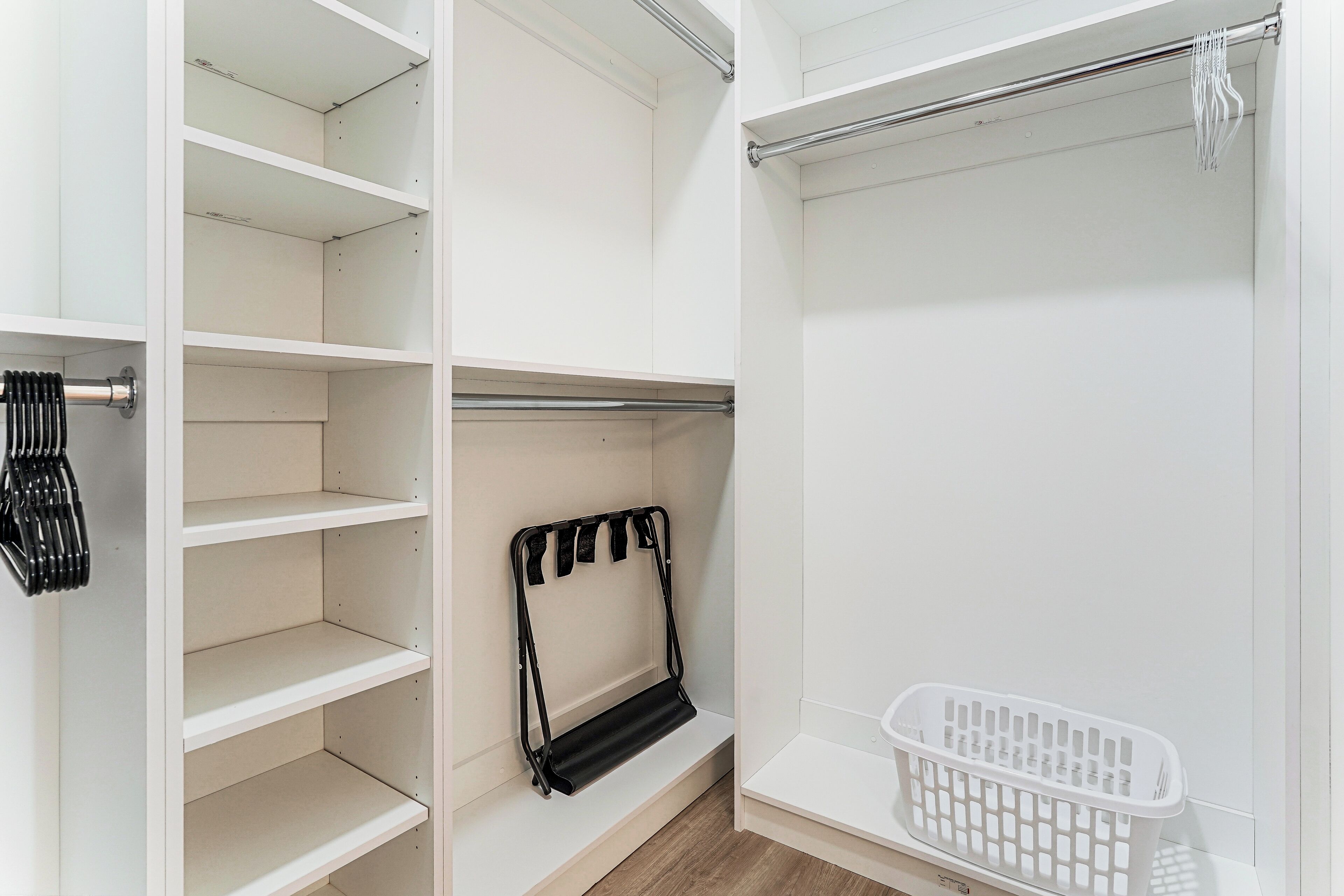 A white closet with open shelves, a black towel rack, and a white laundry basket.