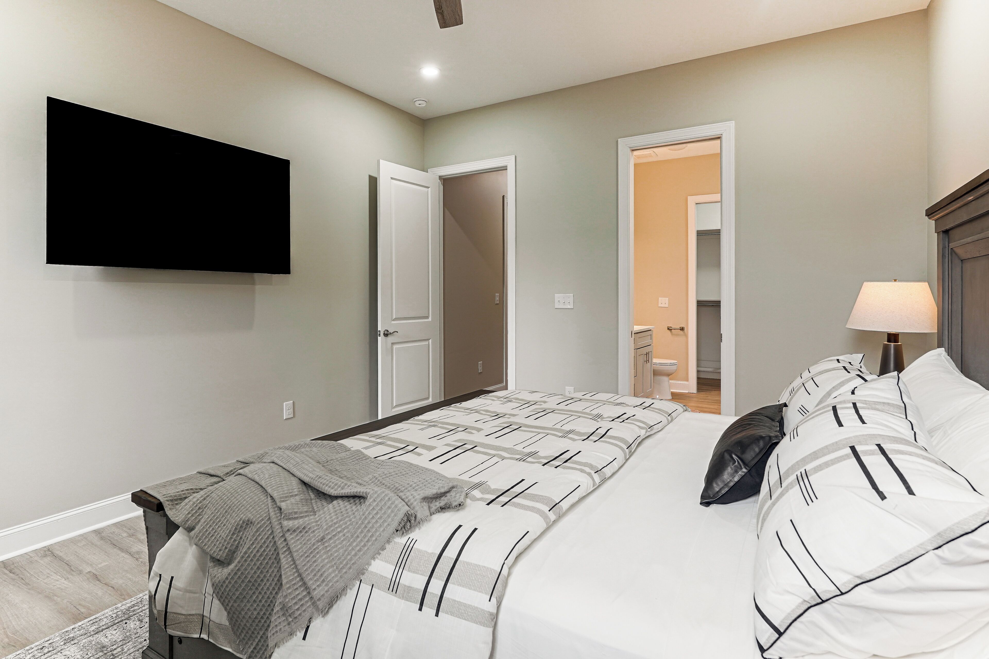 Une chambre à coucher avec un lit, un téléviseur fixé au mur et une porte donnant sur une autre pièce.