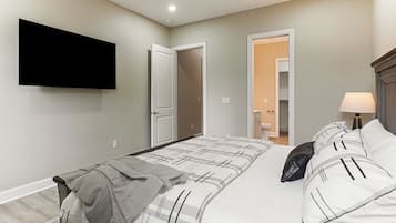 Quarto com cama, televisão fixada na parede e porta que dá para outro cômodo.