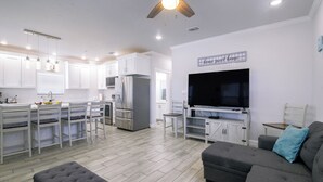 A modern kitchen with white cabinets, a large refrigerator, and a dining area with white chairs. - Private Dock, Pool Access: Oceanfront Cottage (Port Isabel)
