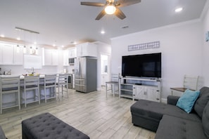 A modern kitchen with white cabinets, a large refrigerator, and a dining area with white chairs. - Private Dock, Pool Access: Oceanfront Cottage (Port Isabel)