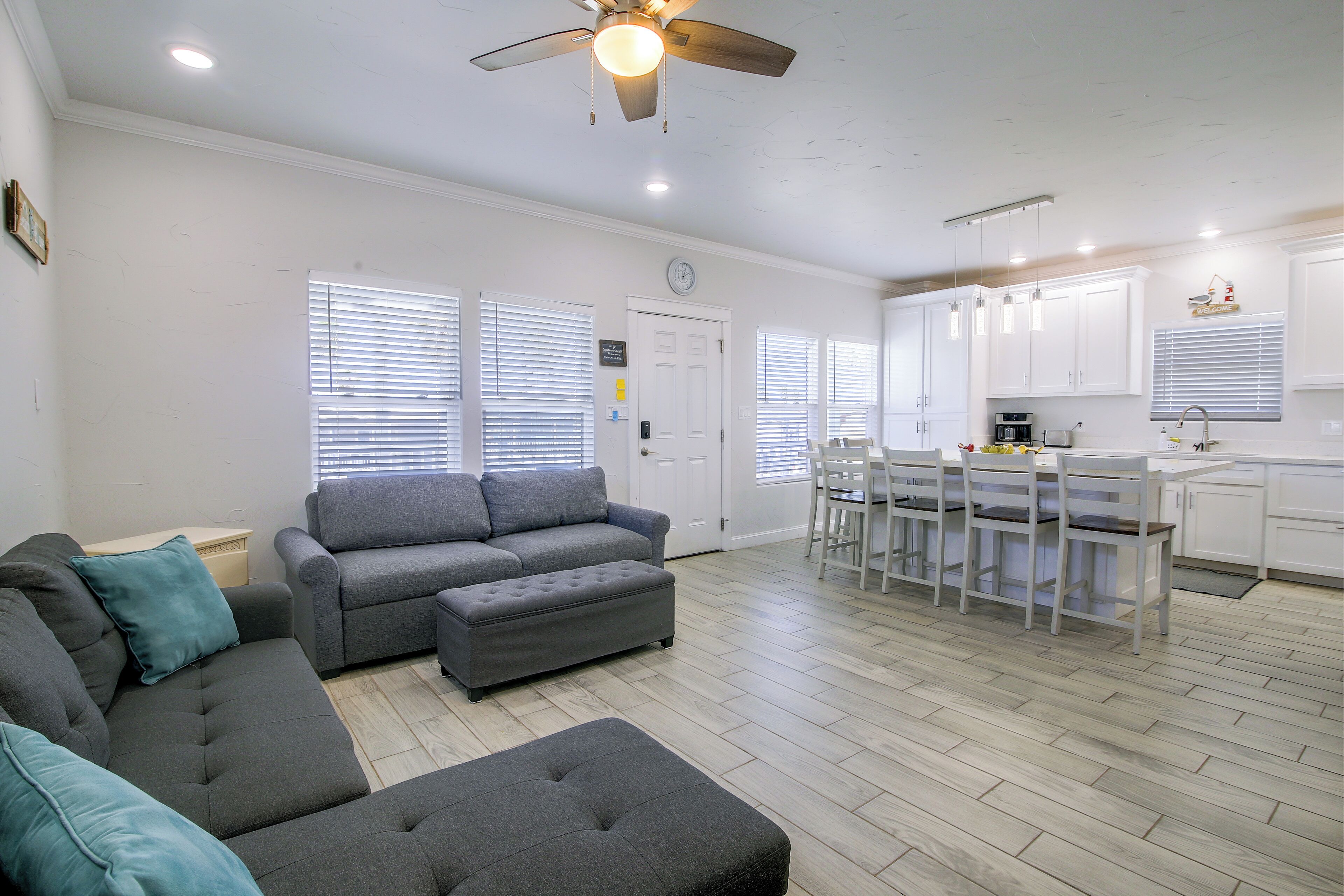 A modern living room with a grey sofa, ottoman, and a ceiling fan.