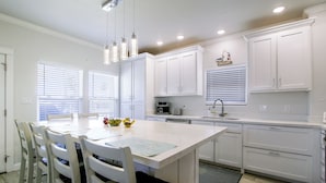 A modern kitchen with white cabinetry, a dining table with chairs, and a kitchen island. - Private Dock, Pool Access: Oceanfront Cottage (Port Isabel)