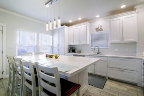 A modern kitchen with white cabinetry, a dining table with chairs, and a kitchen island. - Private Dock, Pool Access: Oceanfront Cottage (Port Isabel)