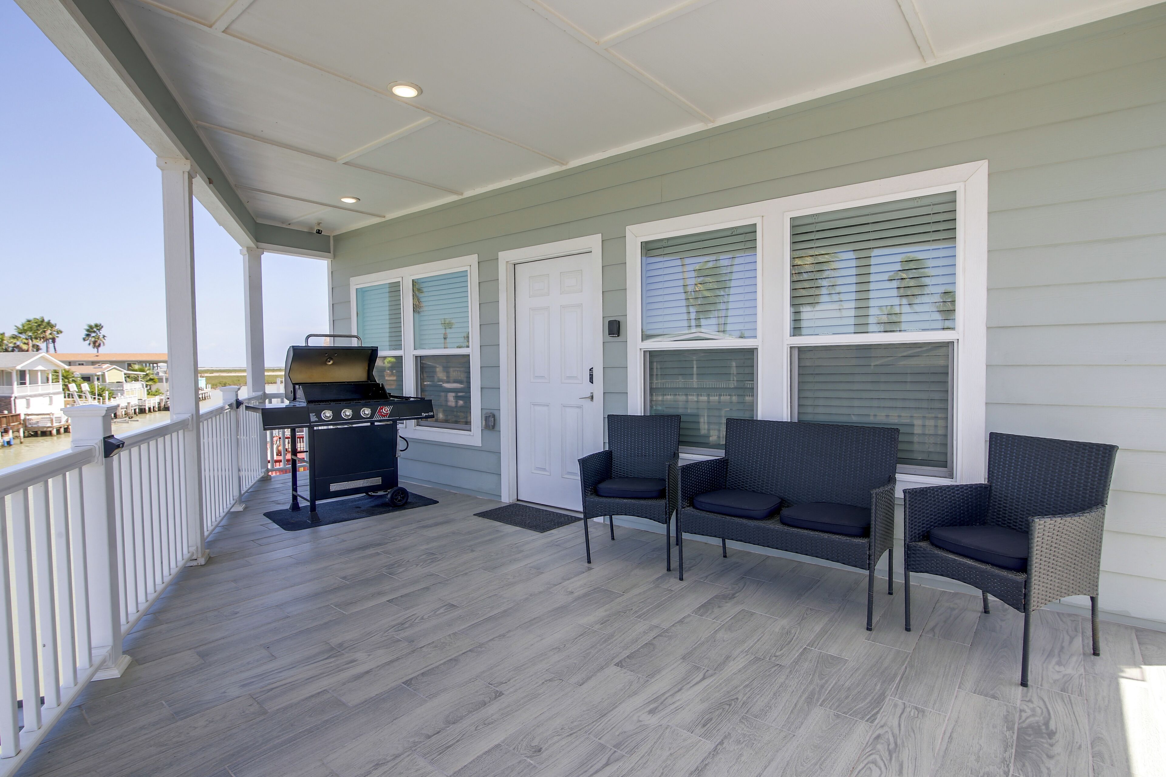 A covered porch with a grill, two chairs, and a view of the ocean.