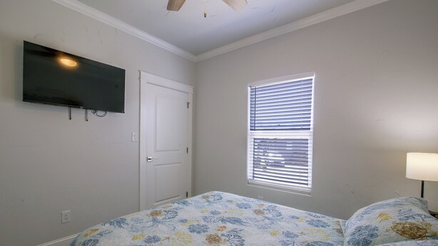 A bedroom with a bed, a television mounted on the wall, a window with blinds, and a door. - Private Dock, Pool Access: Oceanfront Cottage (Port Isabel)