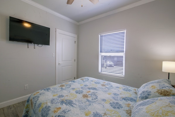 A bedroom with a bed, a television mounted on the wall, a window with blinds, and a door. - Private Dock, Pool Access: Oceanfront Cottage (Port Isabel)