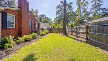 A backyard with a brick house, a wooden fence, and a grassy lawn.