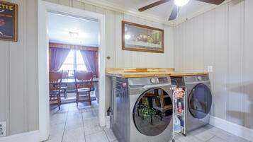 A laundry room with two front-loading washing machines, a ceiling fan, and a dining area with wooden chairs and a table.