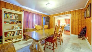 A room with a wooden table, chairs, a bookshelf, and a door leading to another room.